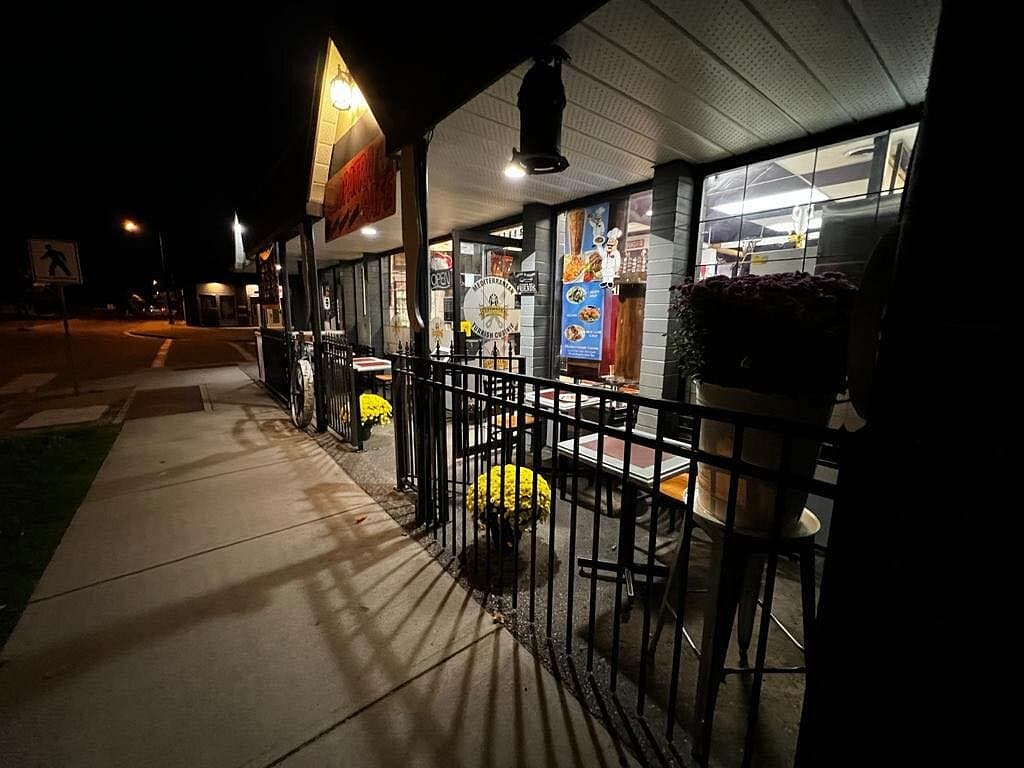 Cleopatra Restaurant at night: illuminated dish photos in the window and the open kitchen glowing inside, wrought-iron patio railing out front