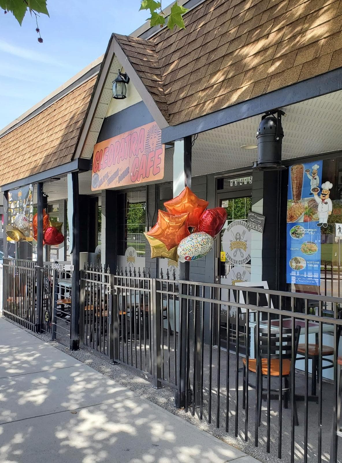 Cleopatra Cafe entrance on a sunny day, wrought-iron patio railing strung with orange and red celebration balloons