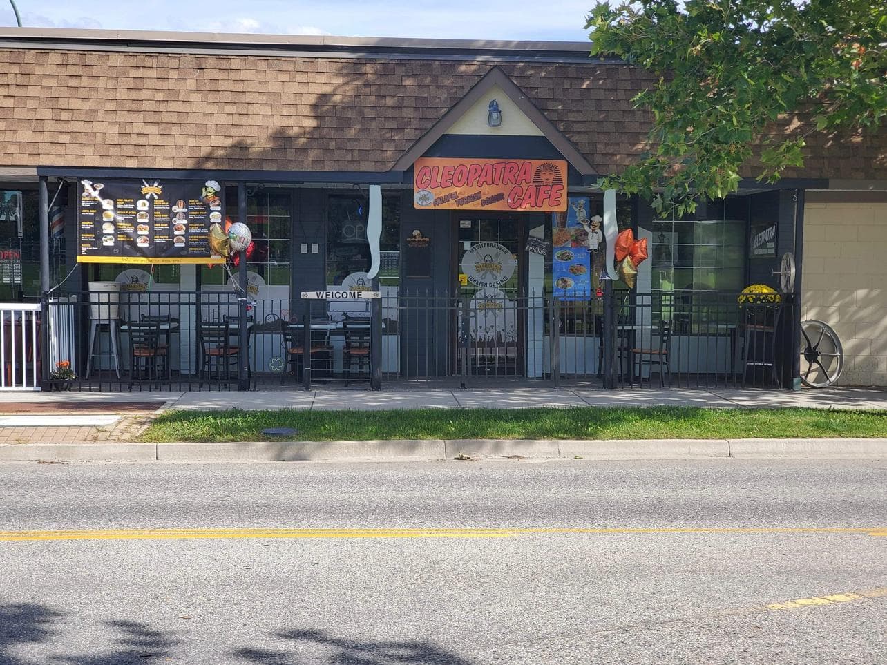 Cleopatra Cafe storefront from across Rosedale Avenue: covered patio seating, illustrated menu boards, and the hand-painted sign